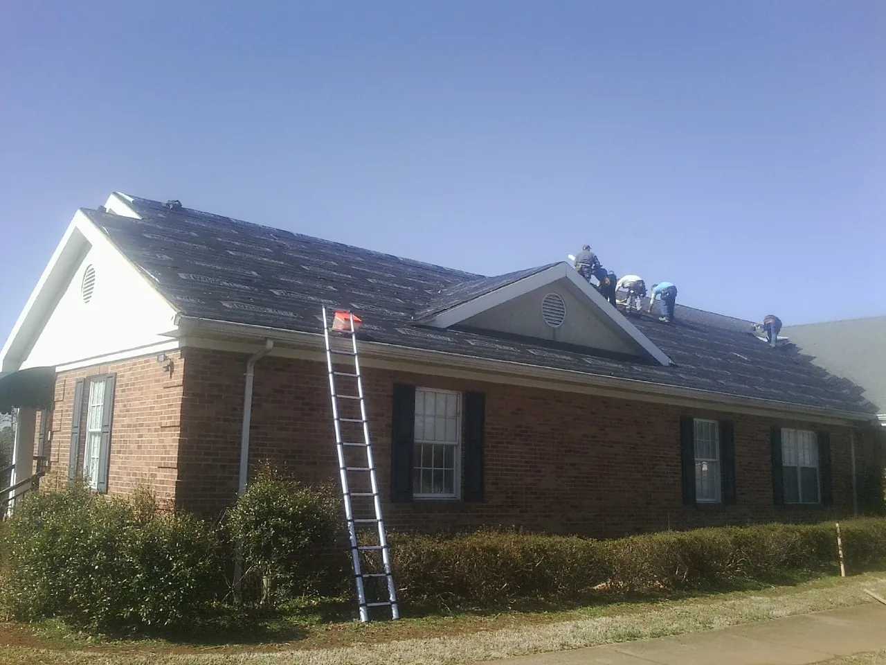 Crew tearing shingles off a brick ranch roof with a ladder set — Metal Roof Repair work by our crew in Clarks Hill