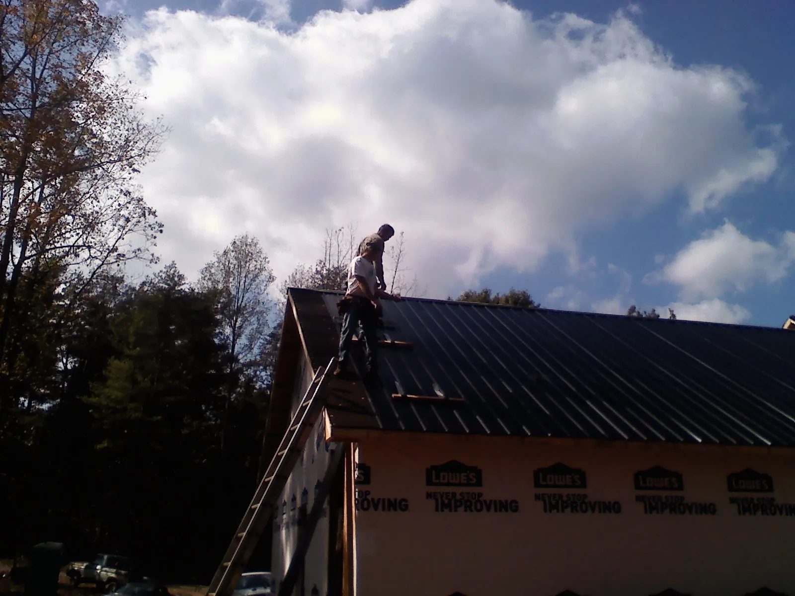 Roofer fastening dark metal panels high against a cloudy sky, from a Roof Inspection job in Clarks Hill