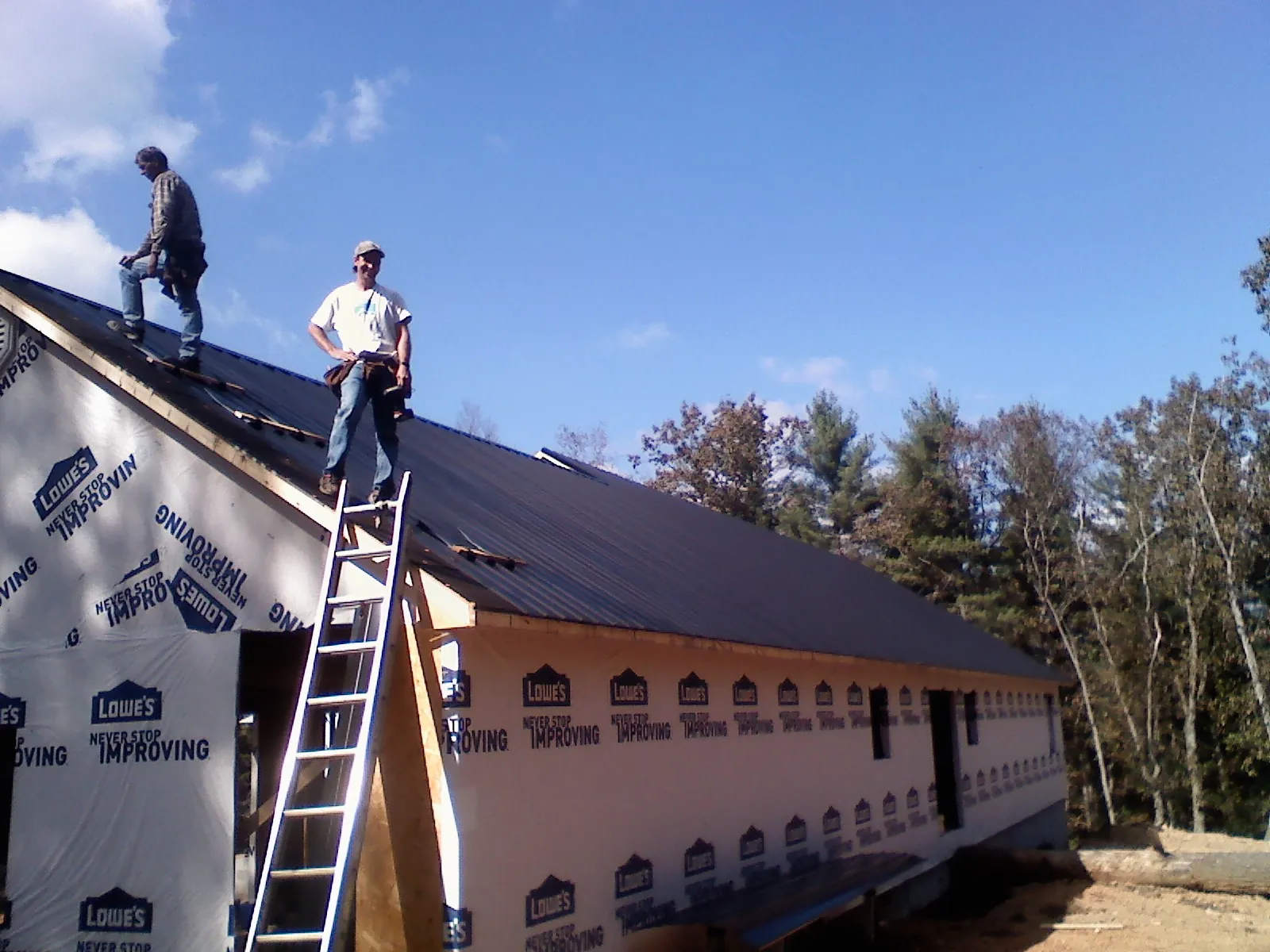 Two roofers standing on a long dark metal roof over a wrapped building in Clarks Hill