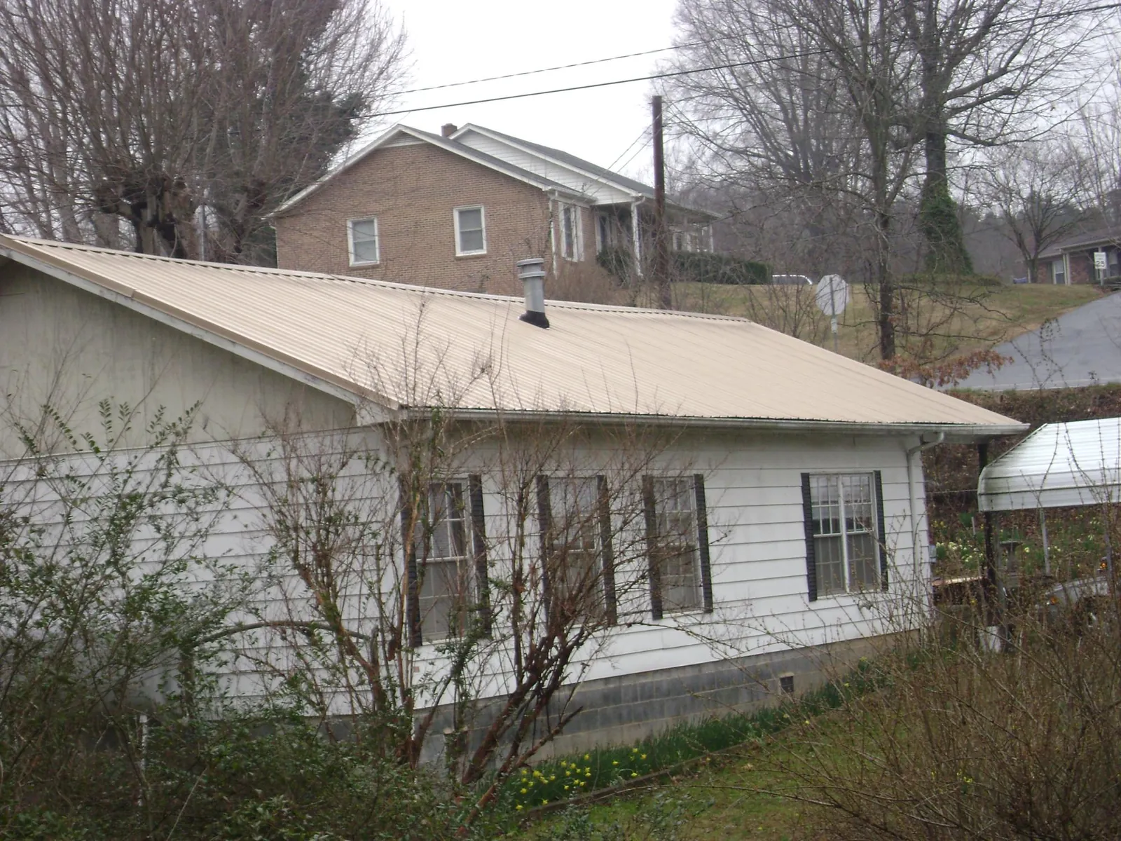Tan metal roof on a white sided house set into a hillside — Commercial Roofing by Roofing Brothers in Clarks Hill